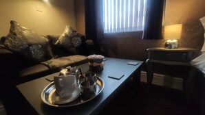 A cozy room with a sofa, a tray with tea set, a lamp, and a window with blinds. - Mardi Gras Hotel (Blackpool)