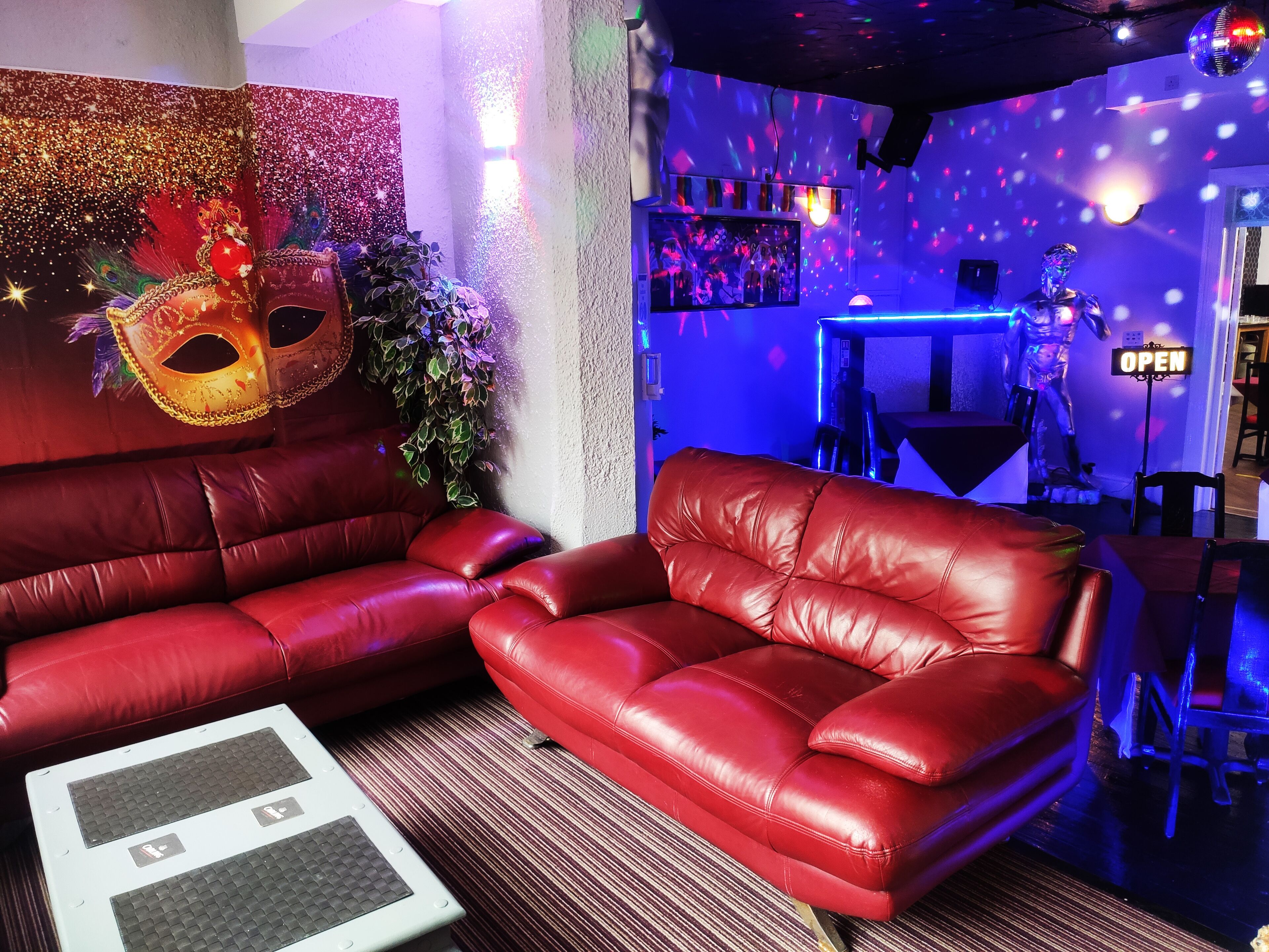 Ein rotes Ledersofa und ein kleiner Tisch in einem Raum mit Discokugel, Spiegel und einem 'OPEN' Schild.