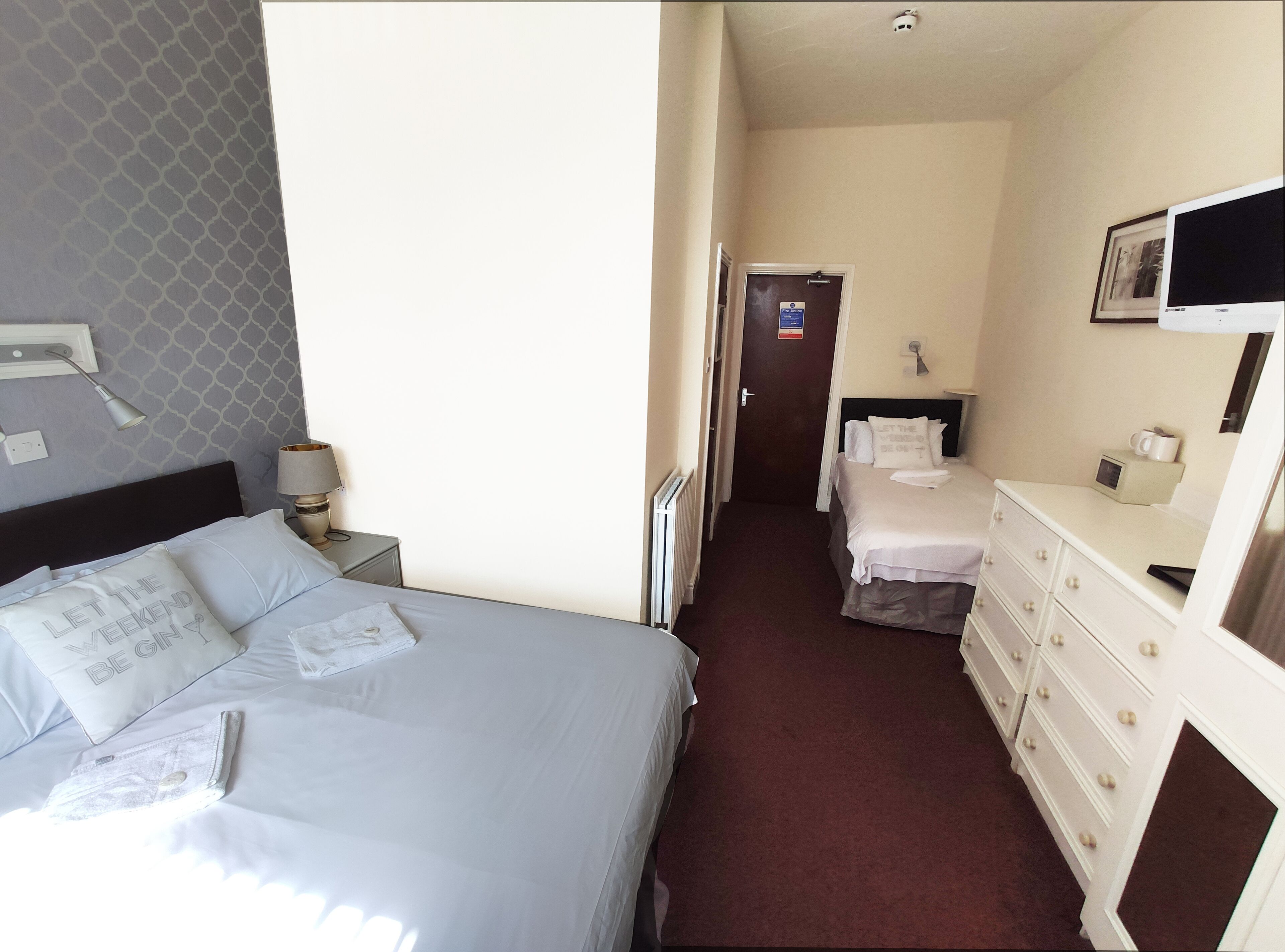 A hotel room with a bed, a nightstand, a dresser, a mirror, and a door leading to a hallway.