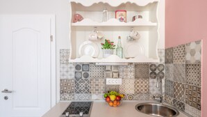 A kitchen with a white countertop, a stainless steel sink, and a fruit bowl. There are patterned tiles on the backsplash and a white door with a handle. - Old City Studios 2 - Adults only (Pula)