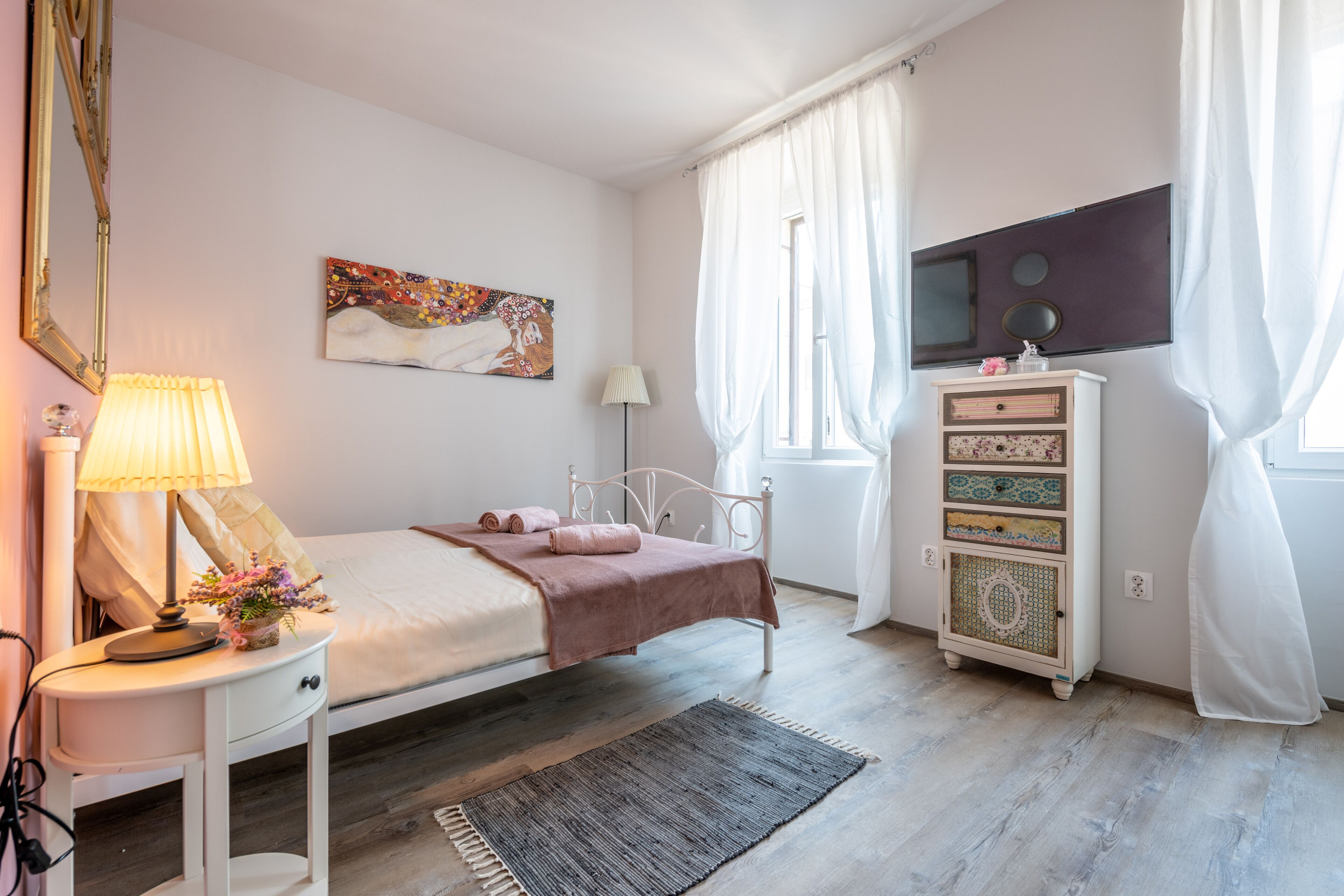 Un dormitorio con cama, mesita de noche, lámpara, cómoda y una obra de arte en la pared.
