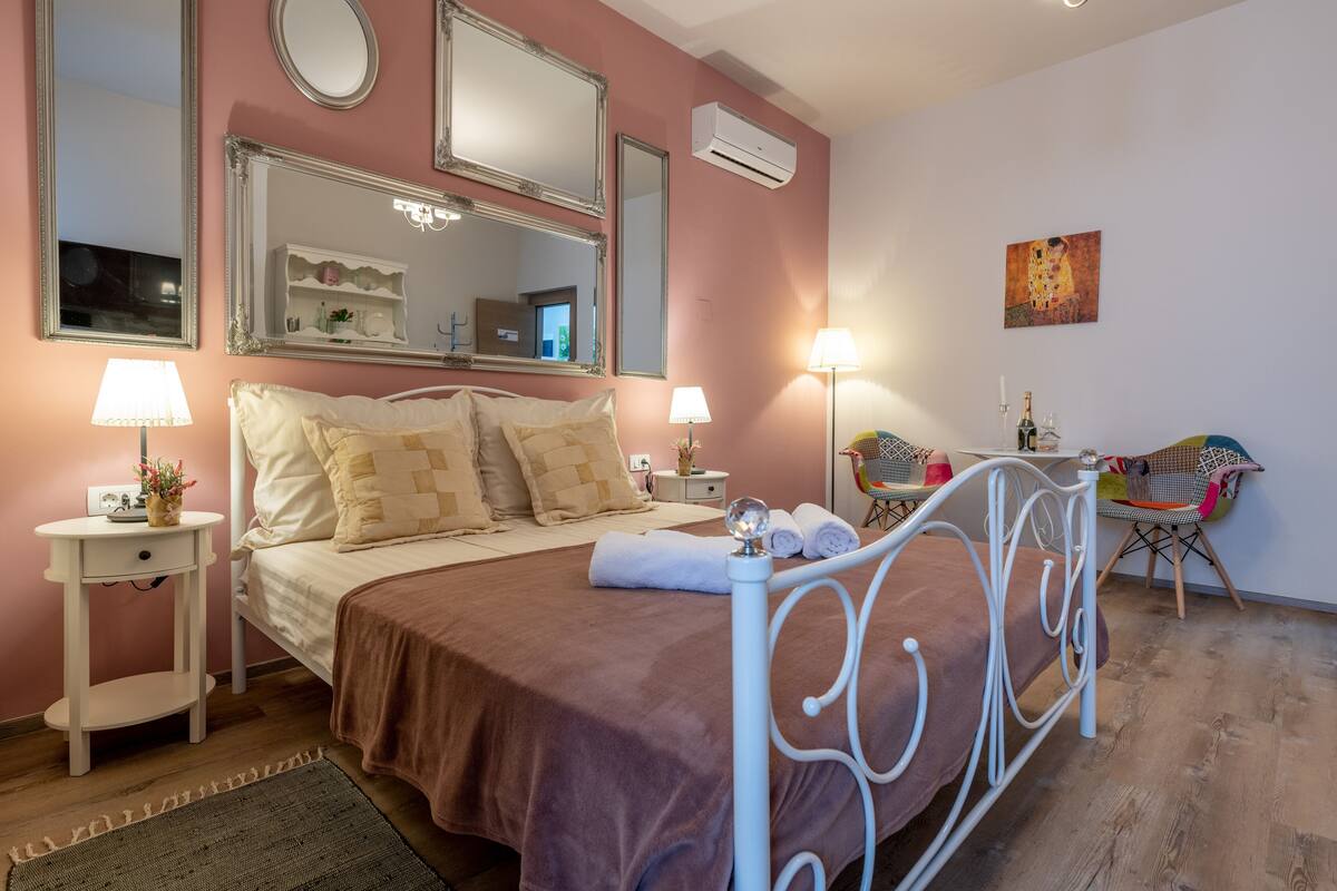 A bedroom with a bed, two bedside tables, a chair, a mirror, and a painting on the wall.