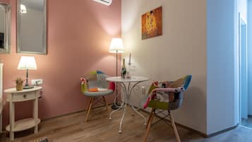 A room with pink walls, a white air conditioner, a table with a lamp, two chairs, and a small white side table with a lamp.