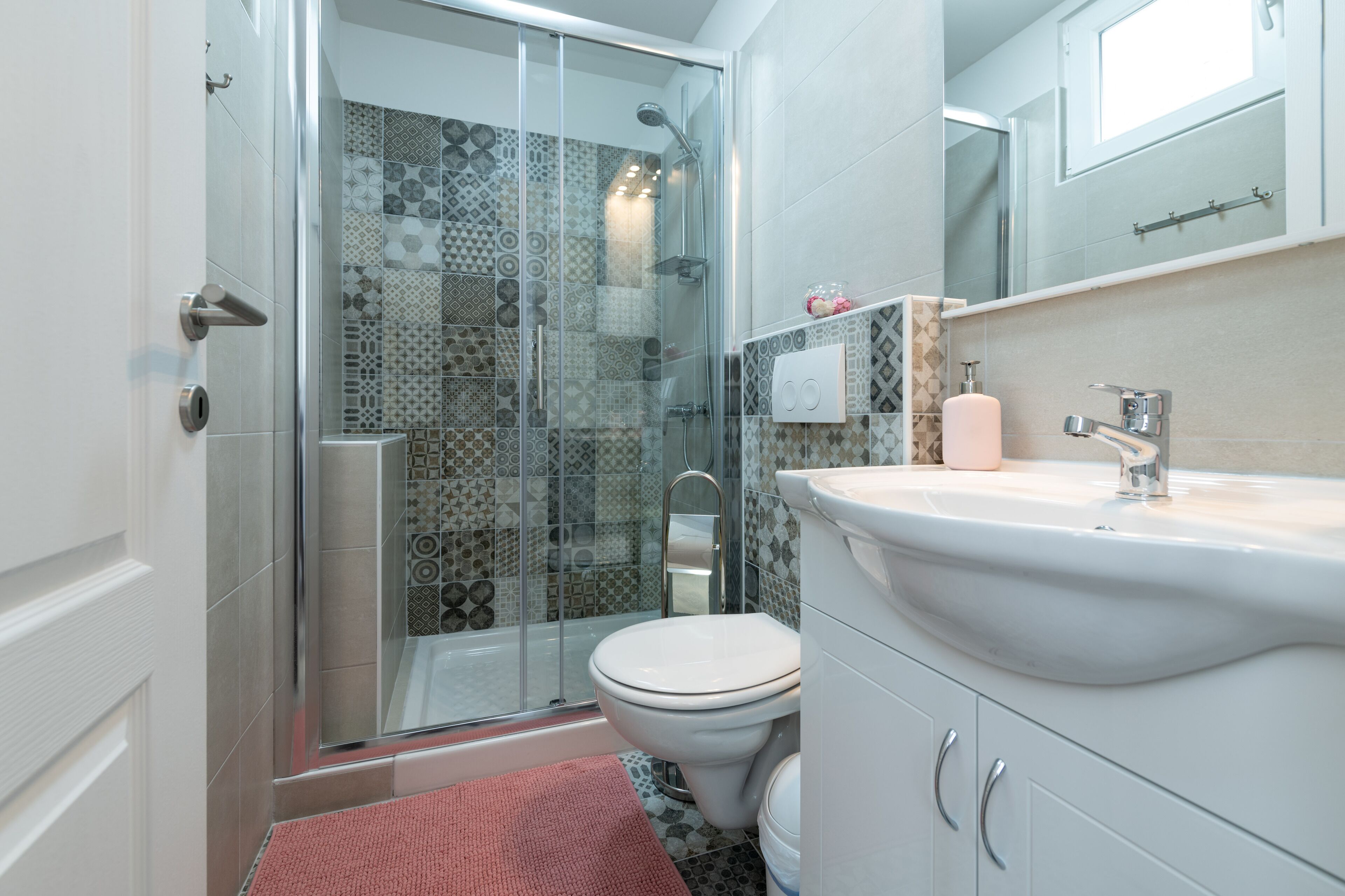 A bathroom with a glass-enclosed shower, a white toilet, and a sink with a mirror above it.