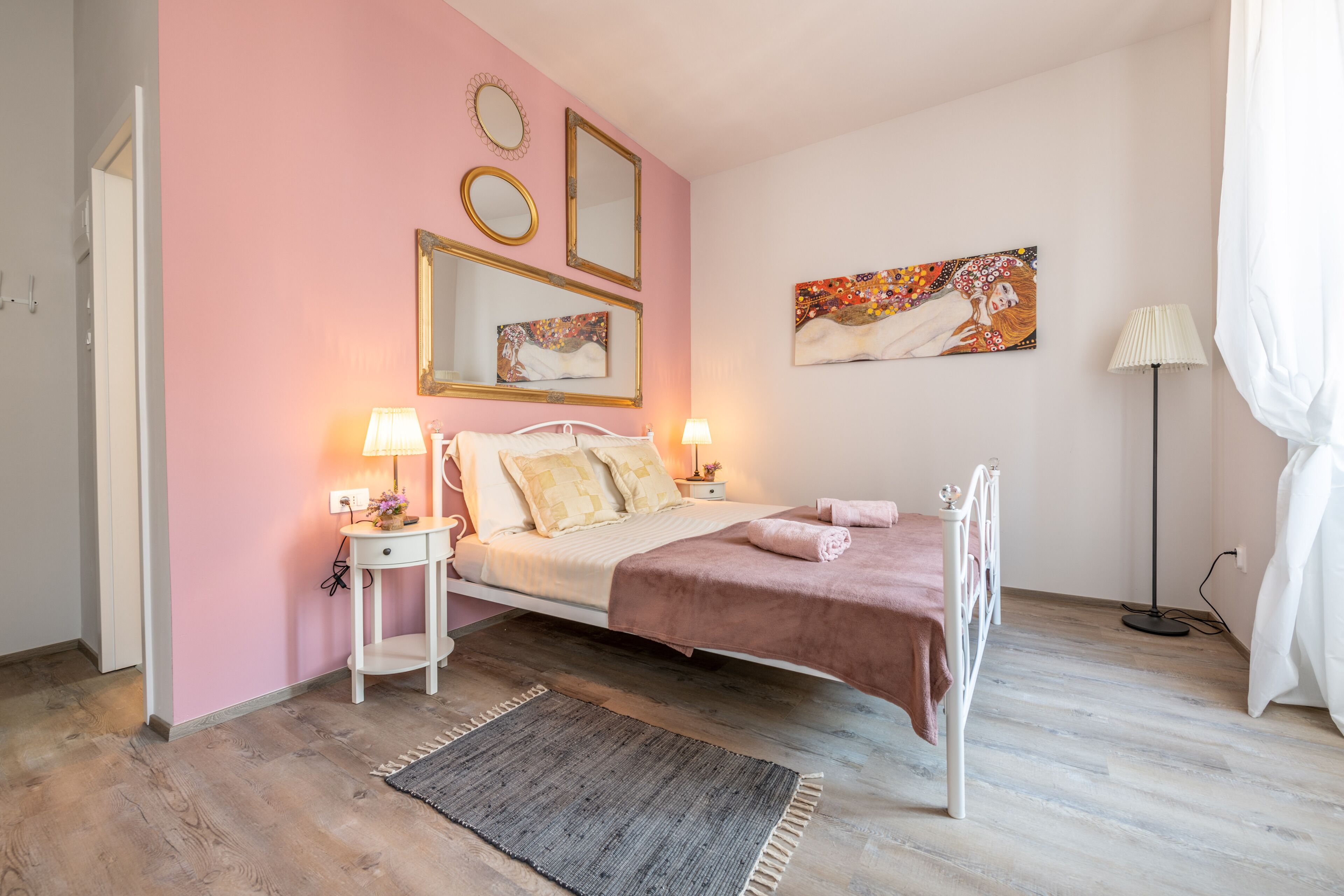 Un dormitorio con cama, mesitas de noche, alfombra y obras de arte en las paredes.
