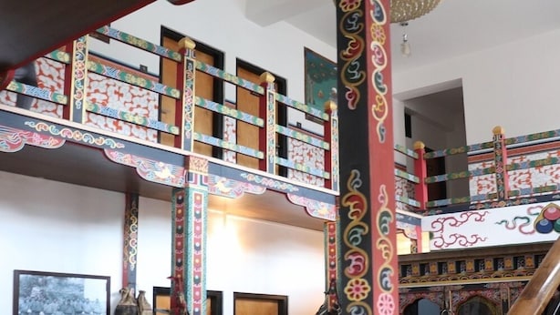 A traditional interior with a wooden staircase, ornate columns, and a patterned rug. - Hotel River Valley (Thimphu)