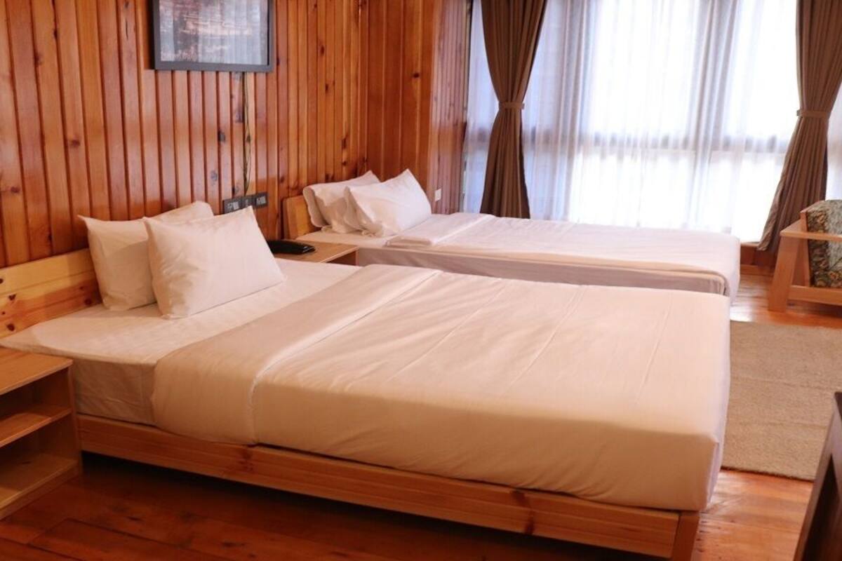 A wooden-paneled room with two beds, a nightstand, and a chair.