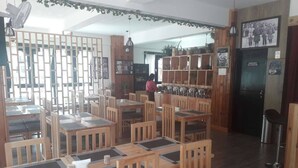 A restaurant with wooden tables and chairs, a counter with food items, and a black door with a sign. - Hotel River Valley (Thimphu)