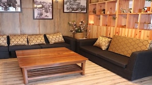 A living room with a sectional sofa, a wooden coffee table, and a wooden wall with shelves. - Hotel River Valley (Thimphu)
