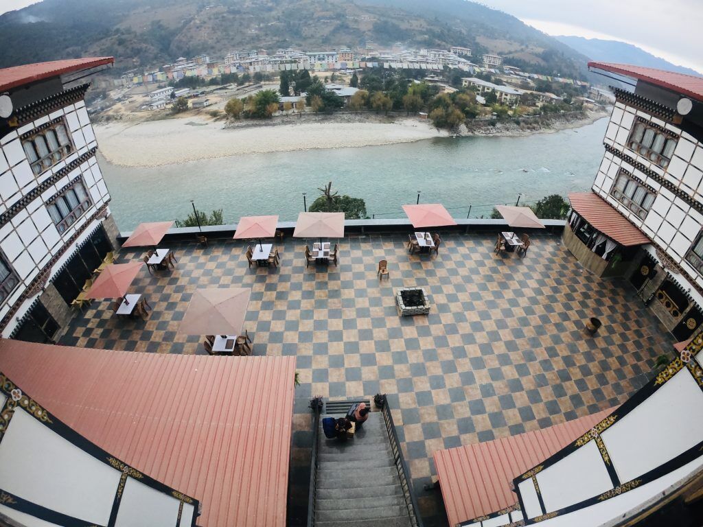 A terrace with checkered flooring, outdoor seating, and a view of a river and distant buildings.