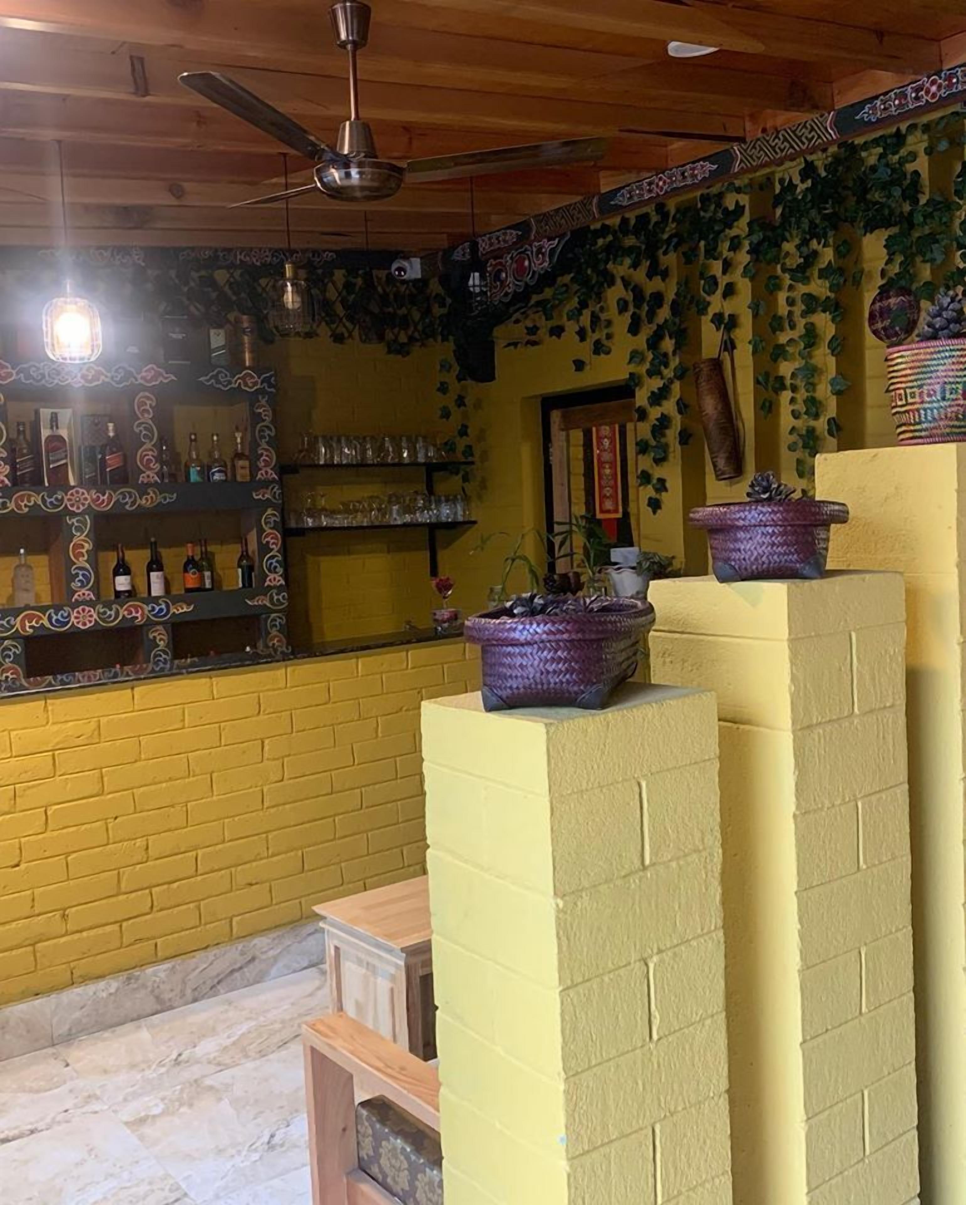 A bar area with shelves of bottles and glasses, a ceiling fan, and decorative plants.