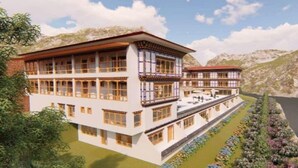 A multi-story building with a flat roof, large windows, and balconies. It is surrounded by mountains and a body of water. - Hotel River Valley (Punakha)