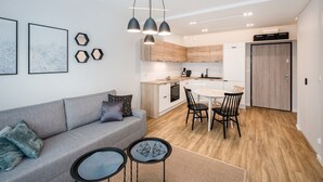 Een modern appartement met een grijze bank, een eettafel met stoelen, een keuken met houten kastjes en een plafondlamp.