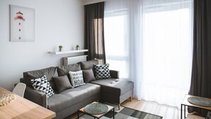 Een moderne woonkamer met een grijze bank, zwart-wit gestreepte kussens, een houten salontafel en een ingelijst kunstwerk aan de muur.