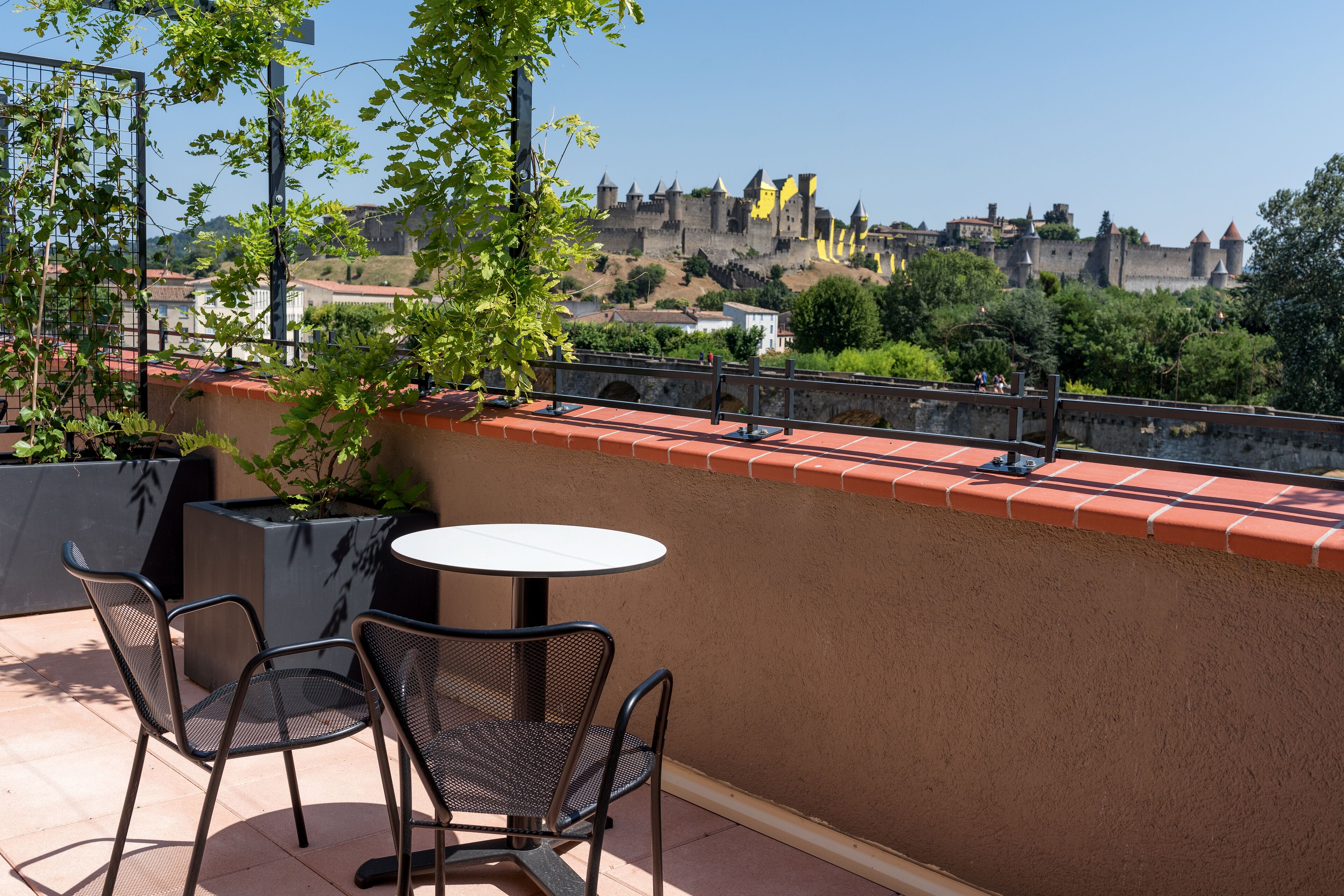 An outdoor patio with a round table and two chairs, overlooking a historic castle and surrounding greenery.