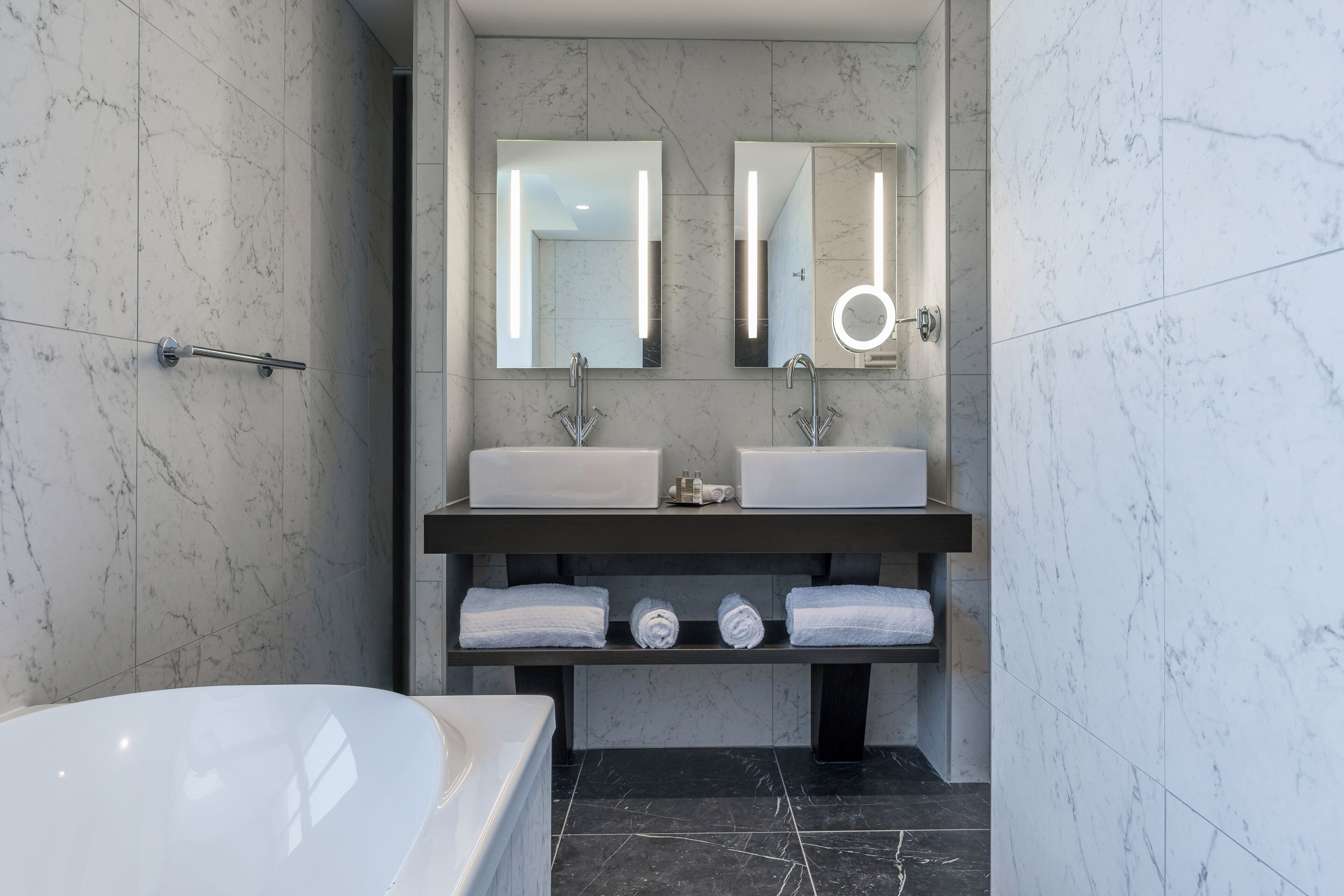 A modern bathroom with two sinks, a large mirror, and a bathtub.