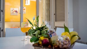 Una mesa con un frutero, un vaso de jugo de naranja y una planta en maceta.