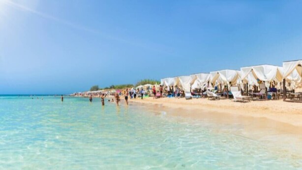 Una playa con agua turquesa cristalina y hileras de tiendas blancas a lo largo de la orilla.