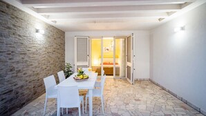 Un patio con suelo de piedra, muebles de mimbre blanco y una mesa dispuesta con frutas y un vaso de jugo de naranja.