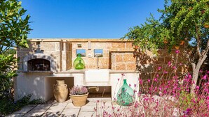 A stone building with a rustic outdoor kitchen area, including a large pot, a green bottle, and a potted plant. - Arcangela Residence - Lentisk with Pool in Salento (Corsano)