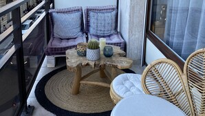 A balcony with a cushioned seating area, a wooden table with decorative items, and wicker chairs. - Small zen and cozy loft with well decorated terrace (Paris)