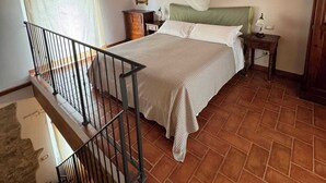 A bedroom with a bed, a nightstand, a bedside table, a ceiling fan, a window with curtains, a wooden staircase, and a tiled floor. - Vinsantaia-Cozy barn on 2 levels (Reggello)