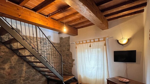 A cozy living room with a stone wall, wooden staircase, a flat-screen TV, and a small wooden table. - Vinsantaia-Cozy barn on 2 levels (Reggello)