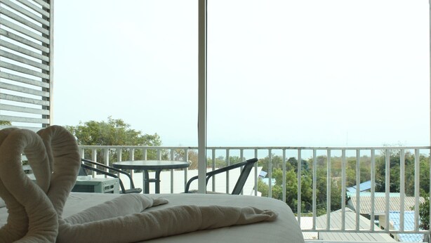 Habitación de hotel con cama, una mesita y balcón con vistas al mar y edificios.