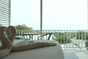 Habitación de hotel con cama, una mesita y balcón con vistas al mar y edificios.
