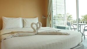 Habitación de hotel con cama, un toalla con forma de cisne, balcón con mobiliario exterior y vista a zonas verdes.