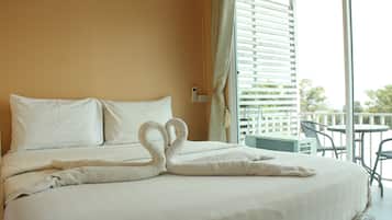 A hotel room with a bed featuring a swan-shaped towel arrangement, a balcony with outdoor furniture, and a view of greenery outside.