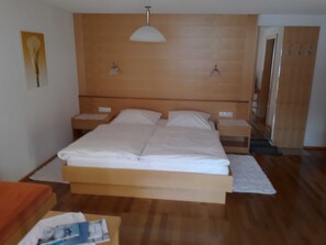 A bedroom with a wooden headboard, a single bed, two bedside tables, a nightstand, a white throw rug, and a wooden door. - Double room new (type A) Z-NR. 4 - Greber Christine - Bed and breakfast (Schoppernau)