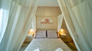 Ein Schlafzimmer mit einem Bett, zwei Nachttischen, einer Wandleuchte und durchsichtigen Vorhängen.