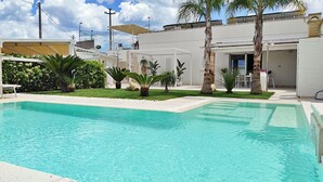 Ein Schwimmbecken mit klarem, blauem Wasser, umgeben von einem gepflegten Garten mit verschiedenen Pflanzen und Palmen.