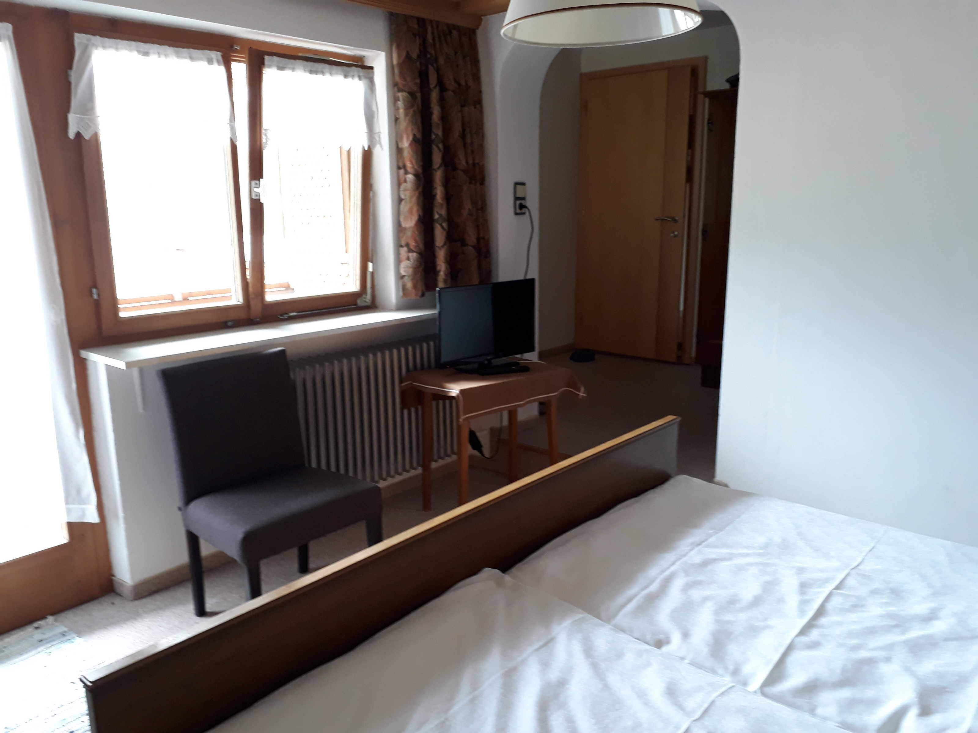 A room with a bed, a desk with a computer, a chair, and a window with curtains.