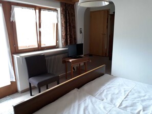 A room with a bed, a desk with a computer, a chair, and a window with curtains.