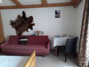 A room with a wooden ceiling, a red sofa, a table with a white tablecloth, and a chair. - Double room (type A) Z-NR. 1 - Greber Christine - bed and breakfast Fernblick (Schoppernau)