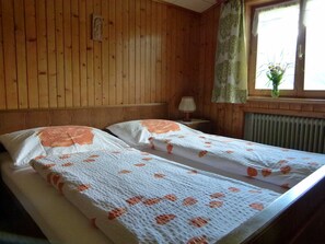 A room with wooden paneling, two beds with floral bedding, a nightstand with a lamp, and a window with a curtain. - Double room (type A) Z-NR. 6 - Greber Christine - bed and breakfast Fernblick (Schoppernau)