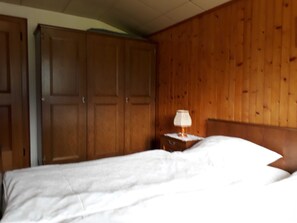 Ein Schlafzimmer mit einem hölzernen Kopfstück, einem Bett mit weißer Bettwäsche und einem Nachttisch mit einer Lampe.