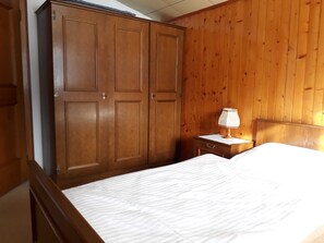 A bedroom with a wooden wardrobe, a bedside table with a lamp, and a bed with a white mattress. - Double room (type A) Z-NR. 6 - Greber Christine - bed and breakfast Fernblick (Schoppernau)