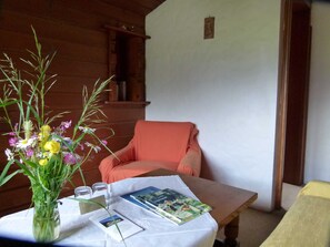 Una habitación con pared de madera, una mesa blanca con un jarrón de flores, una silla y una cama.