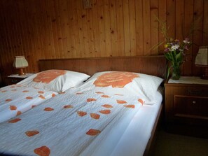A wooden-paneled room with a bed, a nightstand, a lamp, and a vase with flowers. - Double room (type A) Z-NR. 6 - Greber Christine - bed and breakfast Fernblick (Schoppernau)