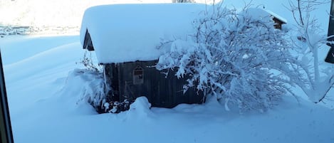 Una cabaña de madera cubierta de nieve, con una chimenea visible y una ventana pequeña.