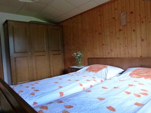 Une chambre avec deux lits, des murs en bois, une armoire en bois et une petite table sur laquelle est posé un vase.
