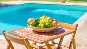 Une table en bois avec un saladier de fruits, placée près d’une piscine.