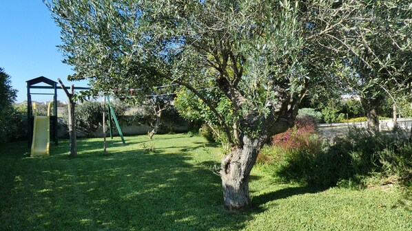 A grassy outdoor area with a swing set and a tree.