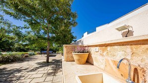 Une terrasse extérieure avec un sol en pierre, une plante en pot, un luminaire fixé au mur et un évier.
