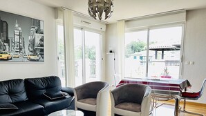 A modern living room with a black leather sofa, two armchairs, a glass coffee table, and a dining table with a striped tablecloth.
