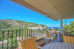 En balkon med stole med gule striber og et bord, der kigger ud over en kystby og havet.
