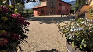 A rustic building with a gravel driveway, surrounded by flowering plants and cypress trees. - Olivaia-beautiful loft apartament with view (Reggello)